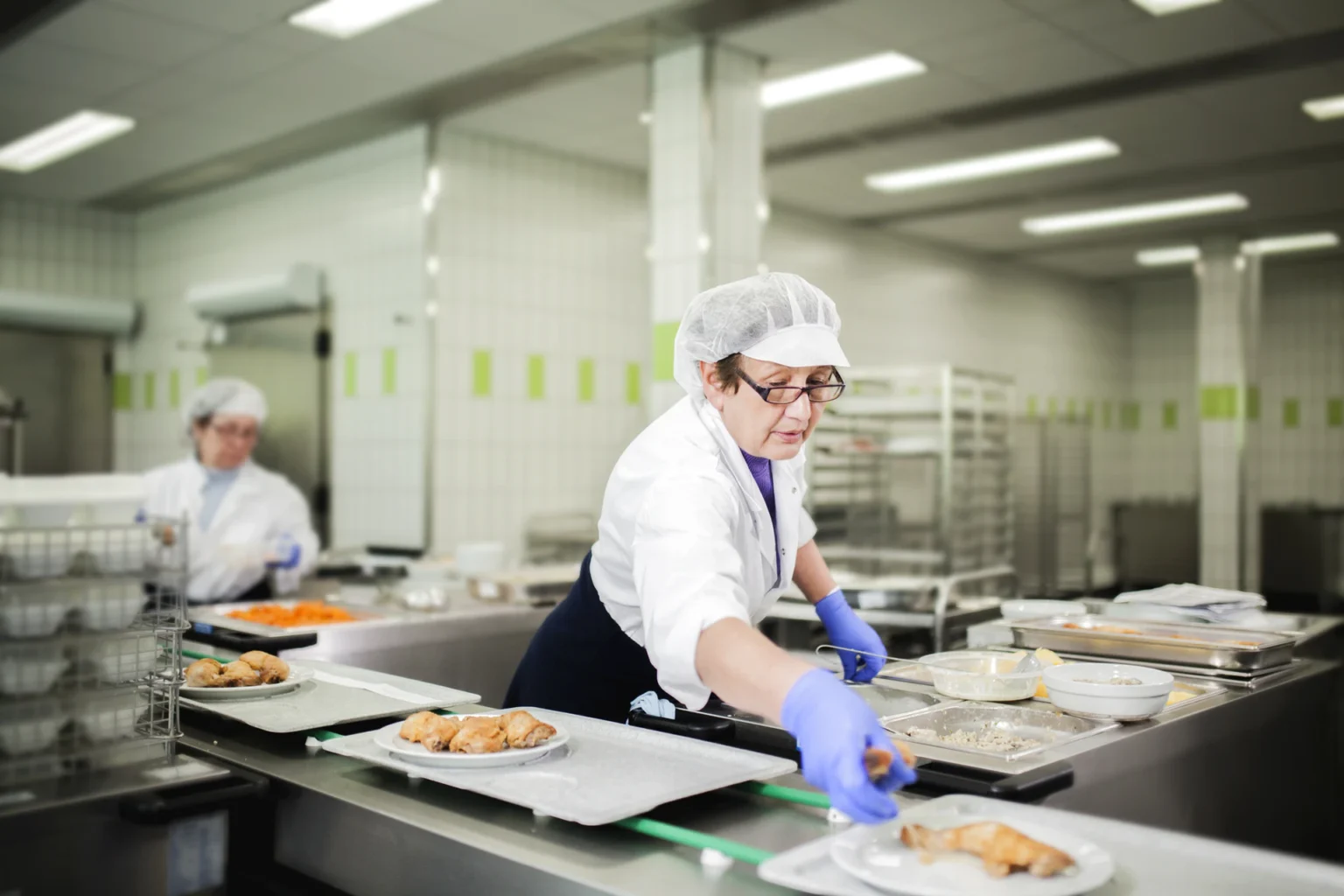 Foto: Küchen-Mitarbeiterin bei der Portionierung von Tellergerichten (© Ernährung-NRW e. V.)